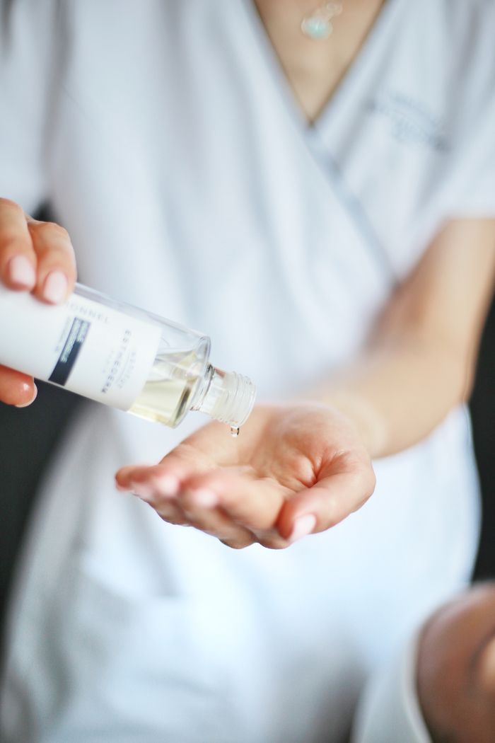 A woman pouring a clear liquid from a bottle into her hand in a close-up, focused shot.