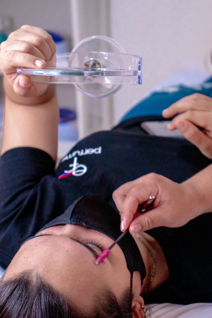 Close-up of a woman lying down receiving an eyebrow care treatment with tools indoors.